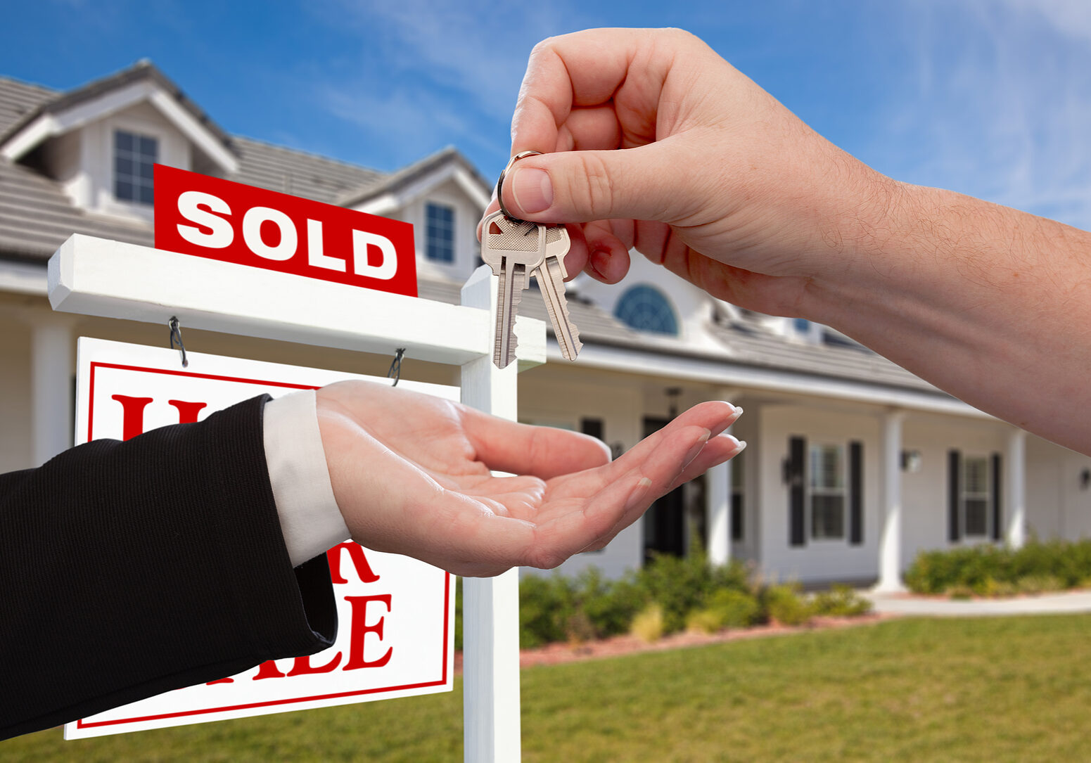 Handing Over the House Keys in Front of Sold New Home Against a Handing Over the House Keys in Front of Sold New Home Against a Blue Sky
